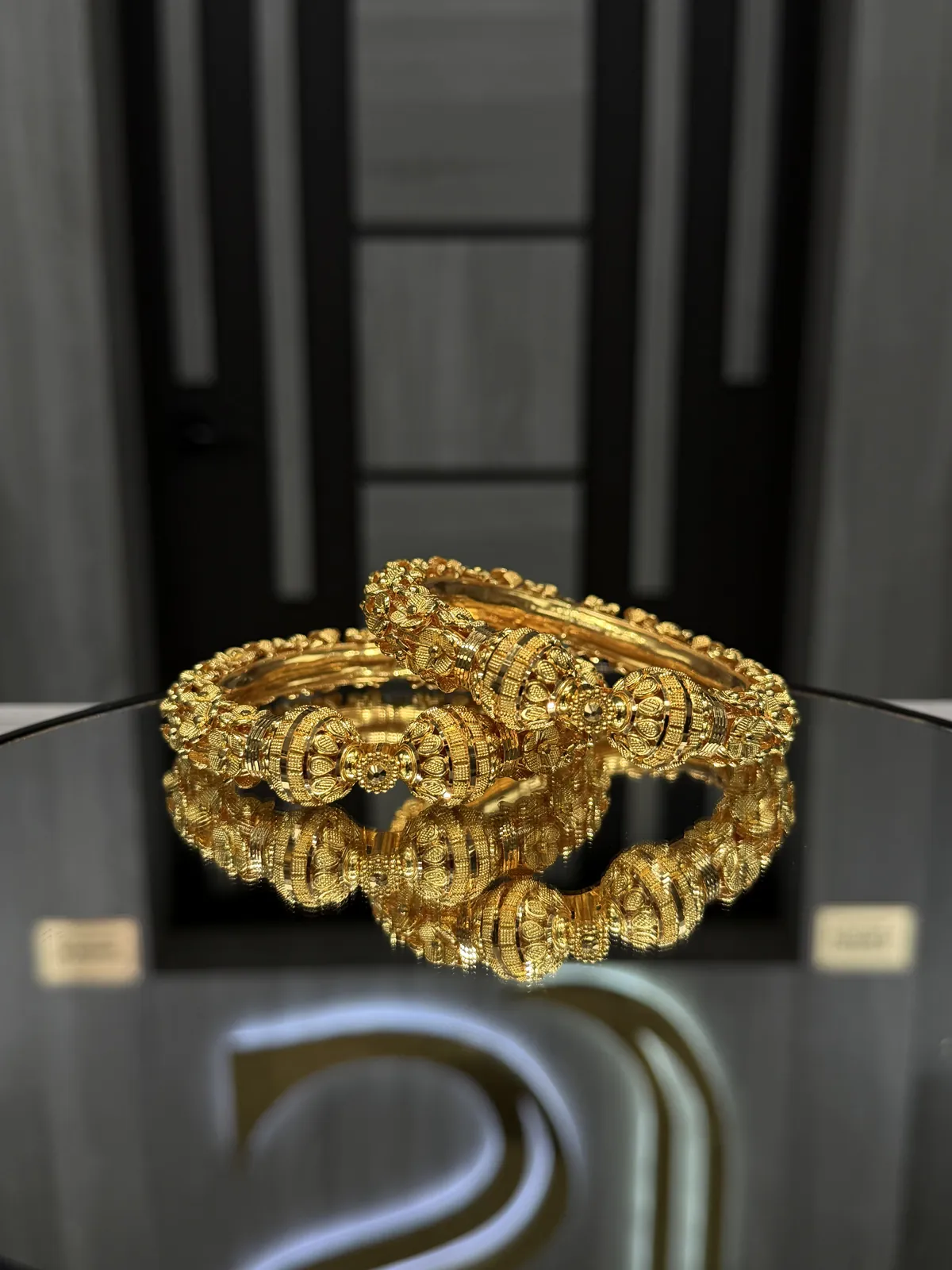 22K gold bangles with ornate beaded floral medallions on a mirrored display table