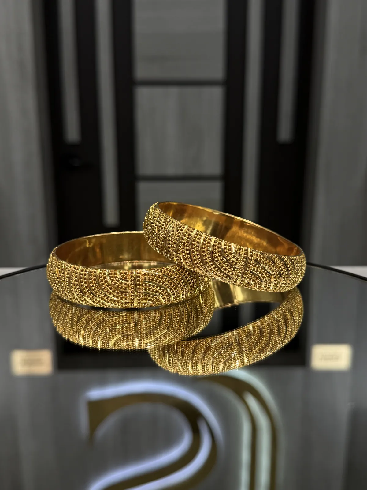 22K gold bangles with a textured swirl and bead pattern on a mirrored display table