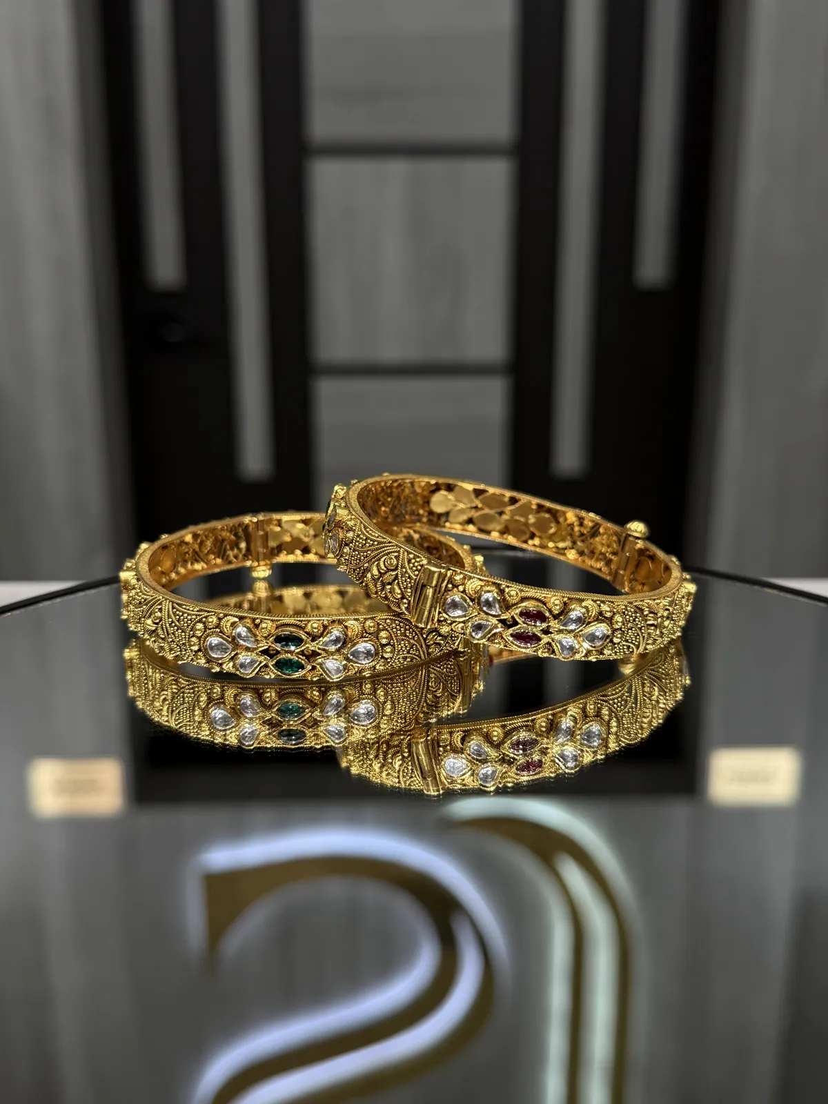 22K gold bangles set with ruby, emerald and clear stones on a mirrored display table