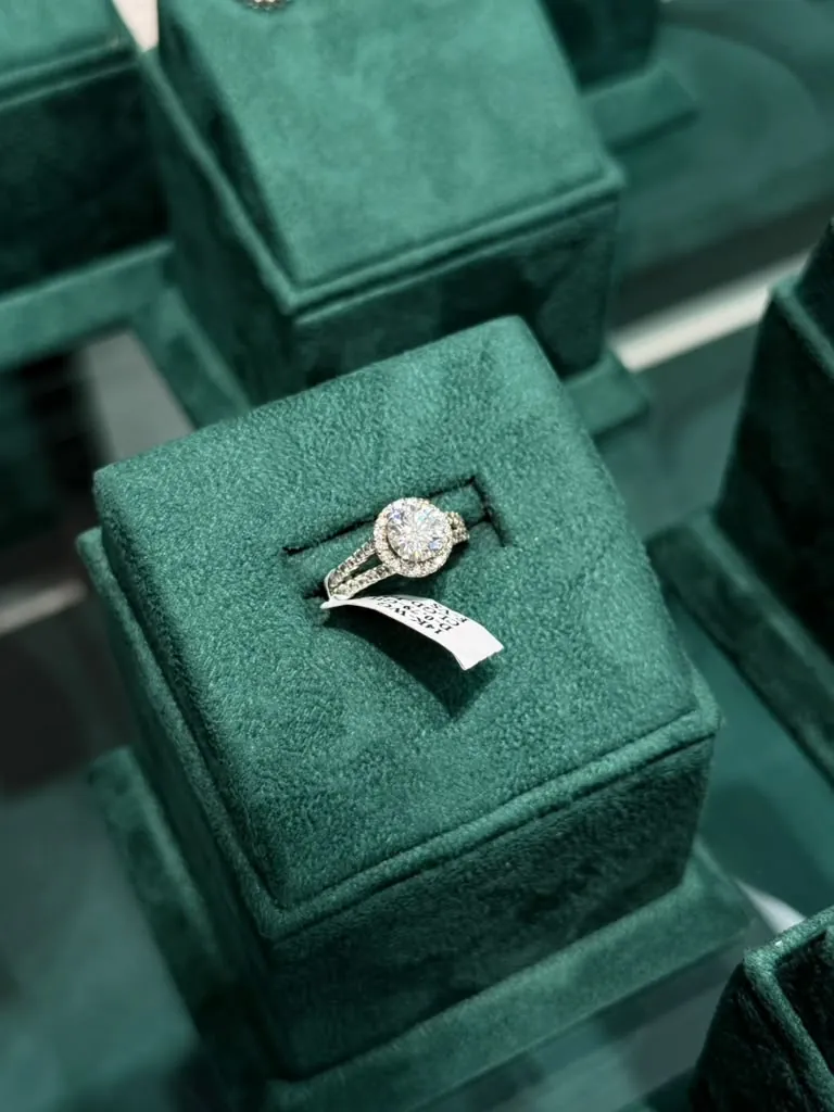 Round diamond halo engagement ring displayed on an emerald velvet ring box