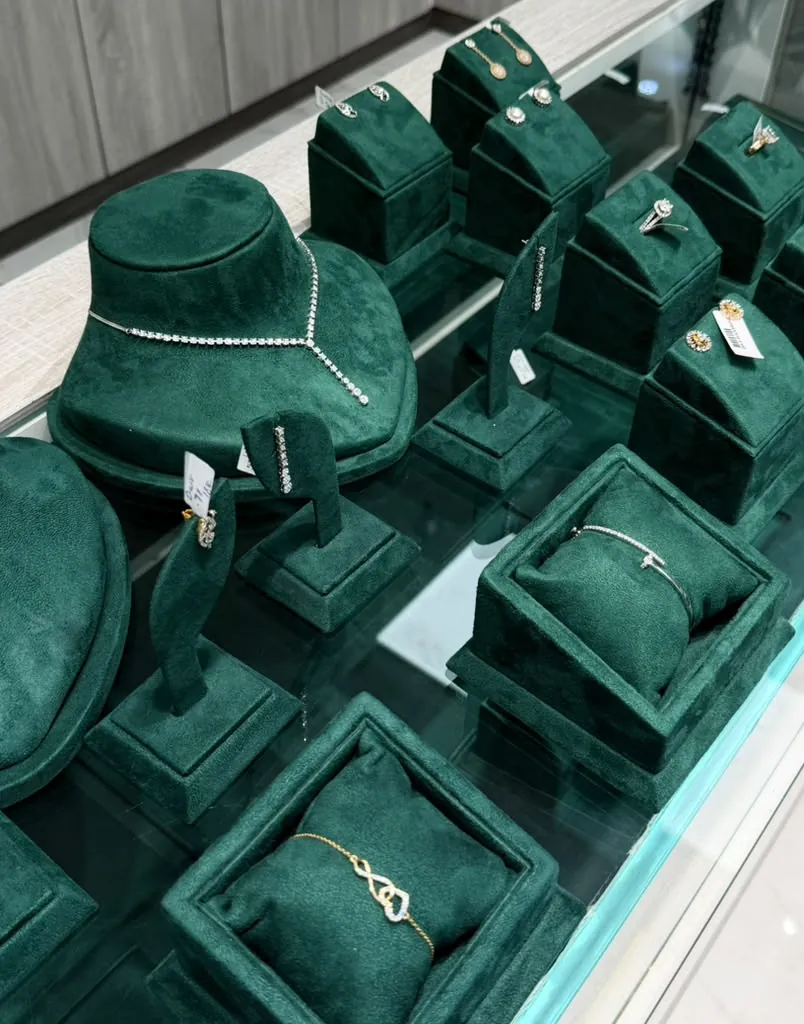 Glass showcase of diamond jewelry on emerald velvet stands — necklaces, rings, bracelets and earrings