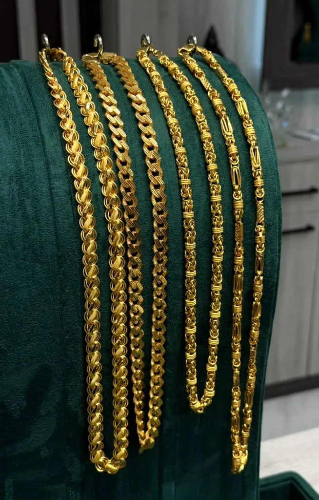 Five statement 22K gold chains with lotus, curb and byzantine links draped on green velvet