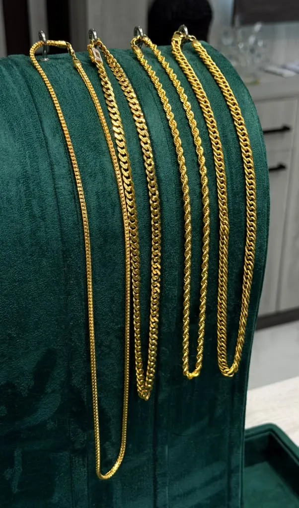 Classic 22K gold chains in franco, curb and rope styles hanging on a velvet display