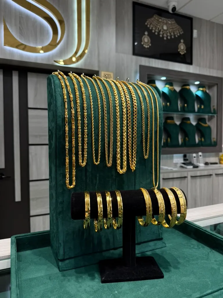 A dozen 22K gold chains in varied link styles draped over a green velvet stand