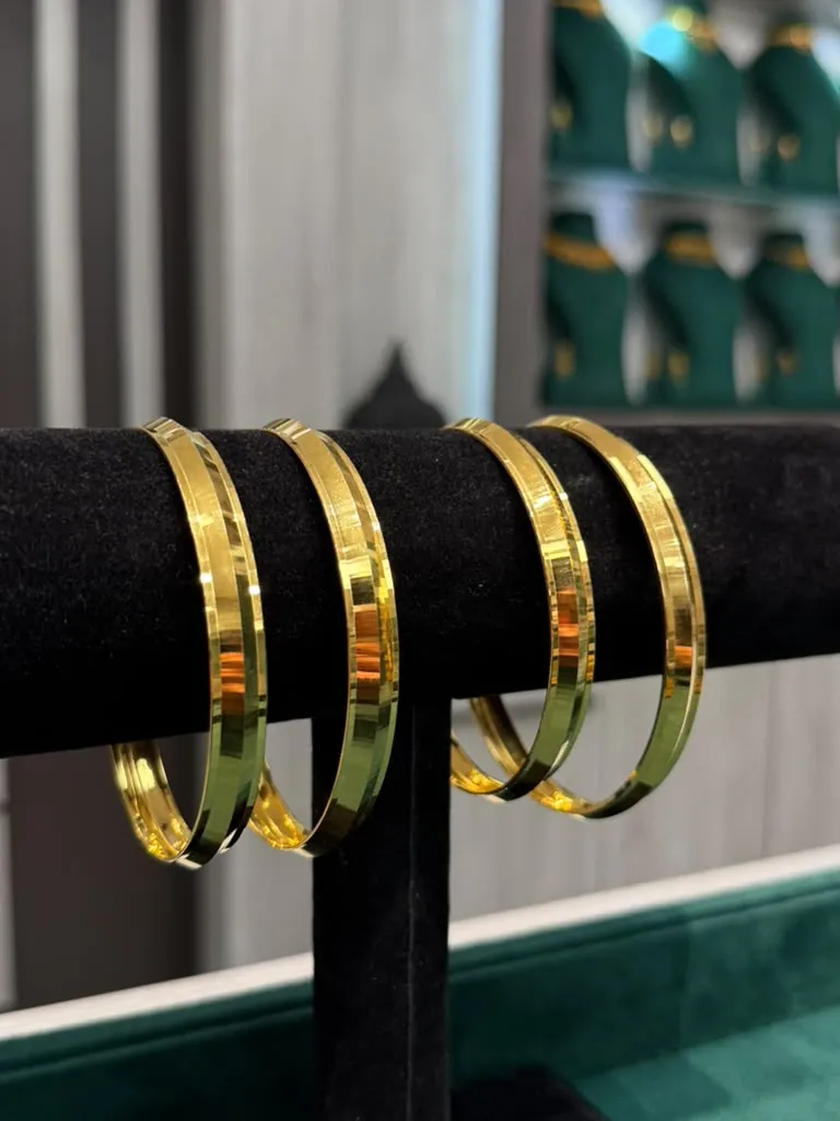 Polished 22K gold kadas with mirror finish resting on a black velvet roll