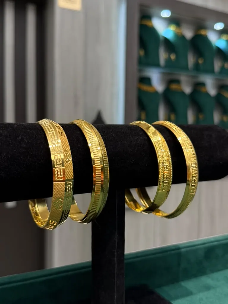 Engraved 22K gold kadas with Greek-key and floral patterns on a black velvet stand