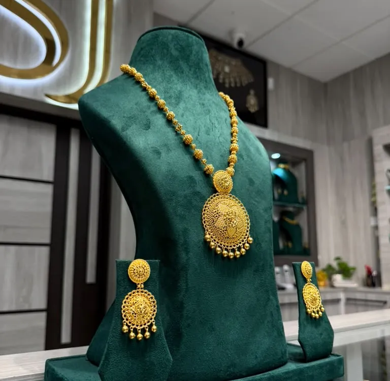 Long 22K gold rani haar necklace with a round filigree pendant and matching earrings on a velvet bust