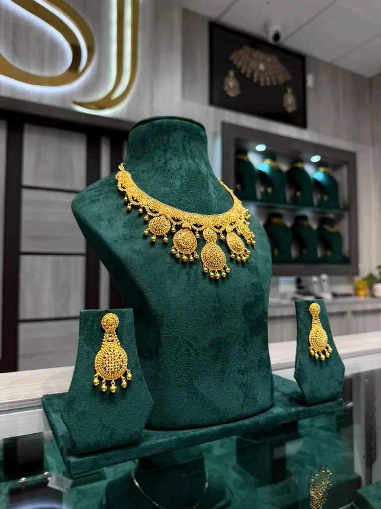 Gold necklace with teardrop medallions and matching chandelier earrings on green velvet stands