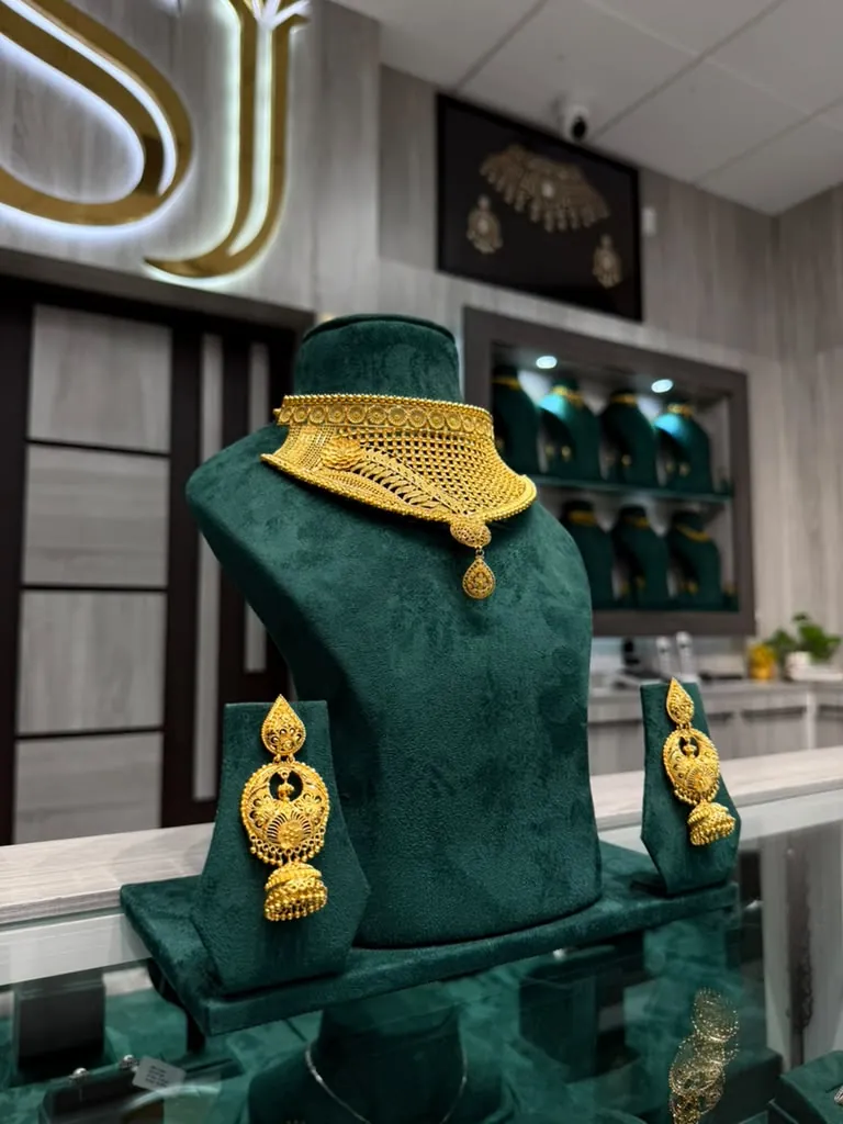 22K gold choker set with matching jhumka earrings on a green velvet bust in the Sai Jewelers showroom